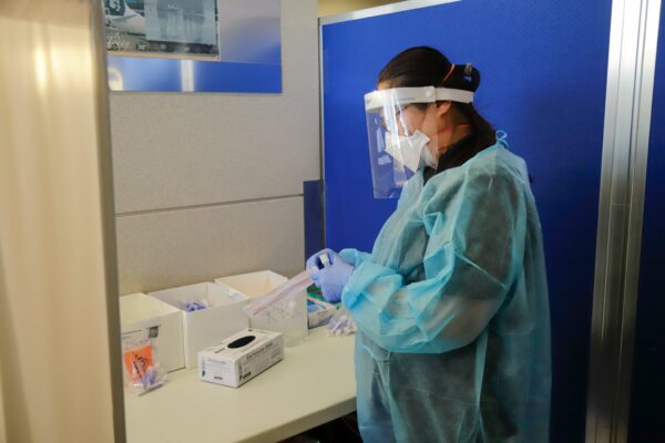 a Covid-19 swab specialist in medical gown, face mask, and face shield prepares to swab a traveler