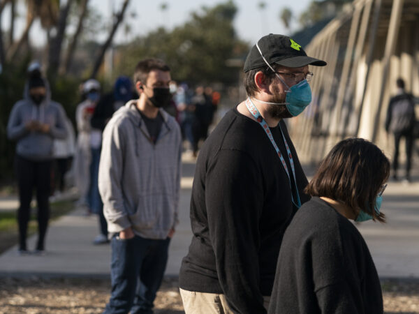 A person in a black baseball hat stands in line with a blue mask