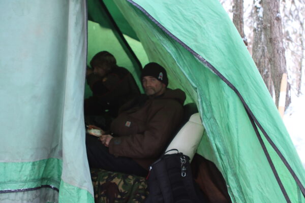 A man in a hat and jacket inside a green tent