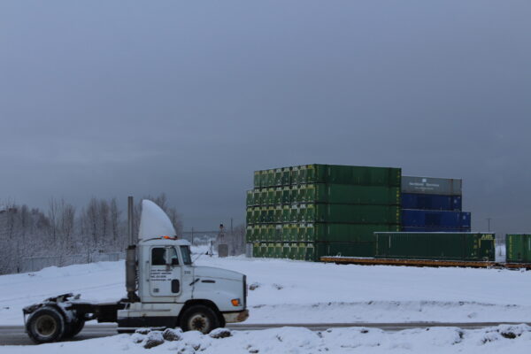 A white truck cab without any cargo on a snowy road with cargo containers stacked behind it