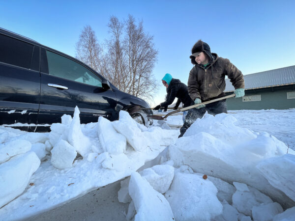 People shoveling snow around a car.