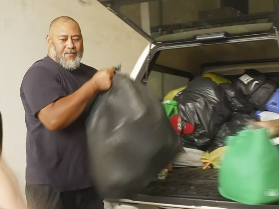 A man takes trash bags out of a trunk of a car.