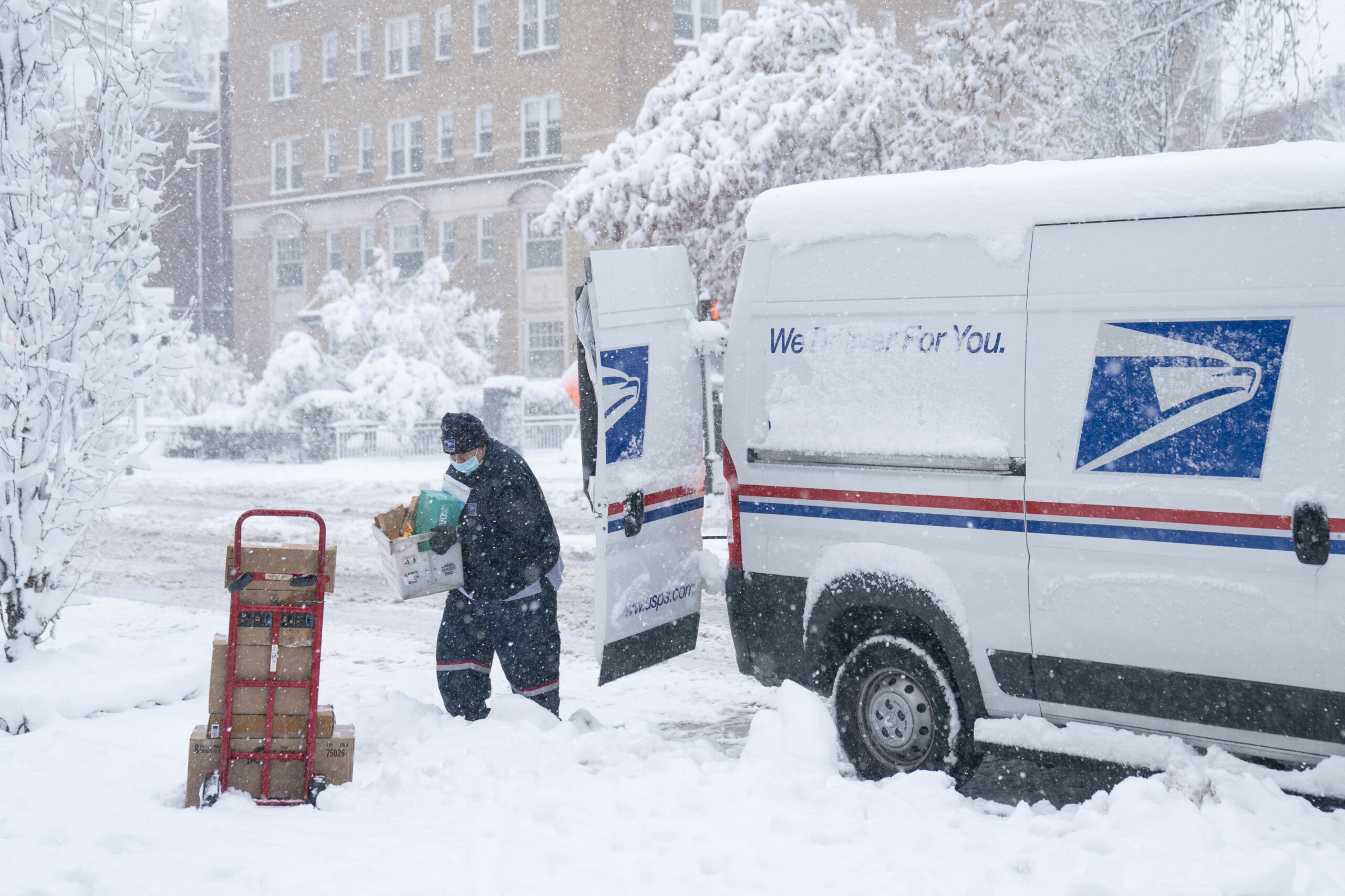 A postal worker carries a package out of his truck in the snow