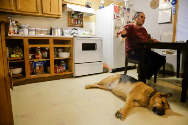 a person at a kitchen table points to the left and his dog lying on the ground