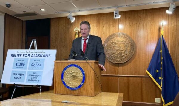 Gov. Dunleavy stands behind a lectern next to a sign that says "relief for Alaskans"