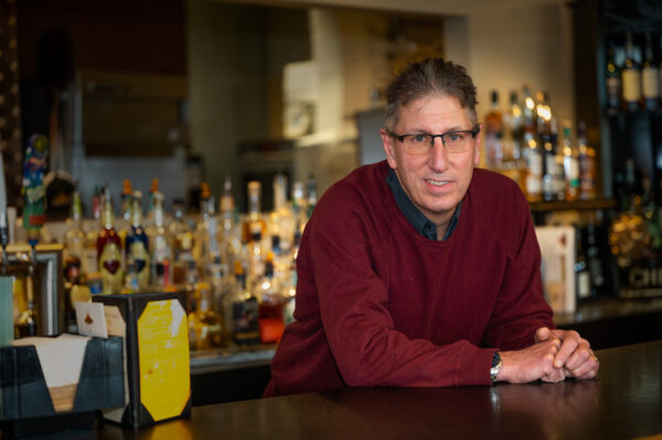 A white man in a red sweater leans over a bar at a restaurant.