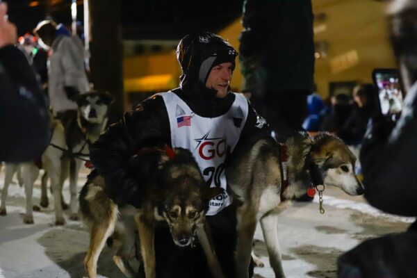a musher poses with two dogs
