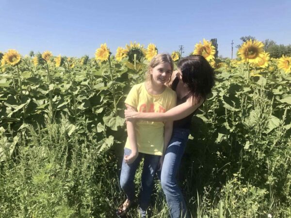 A mother and her teenaged daughter hug in a field of sunflowers