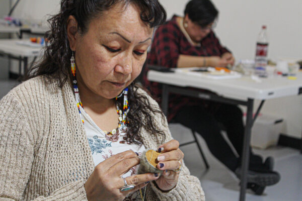 An Alaska Native woman stitches some pieces of leather