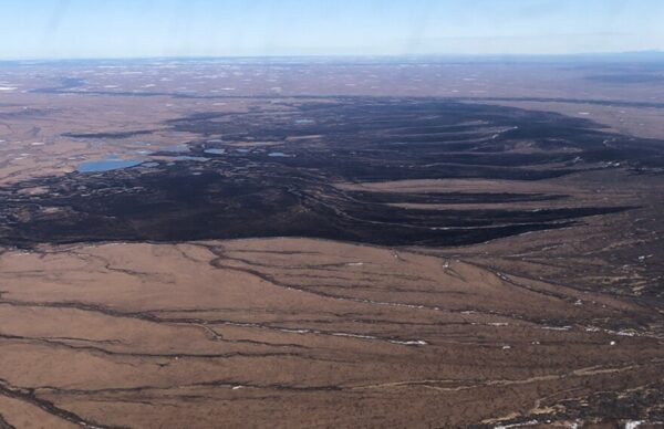 An aerial photo of a brown tundra landscape with a large blackened area where the fire burned
