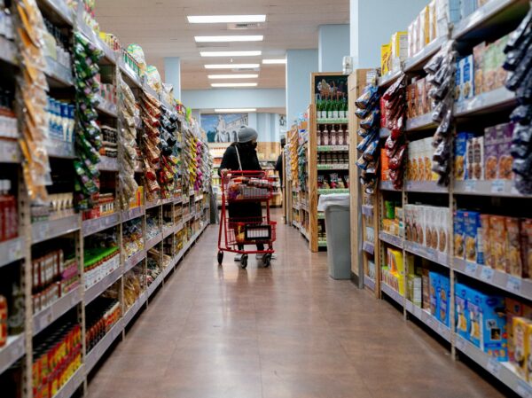 A shopper wheels a shopping cart down a supermarket aisle
