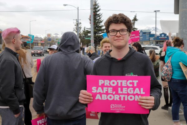 a person stands with a "protect safe and legal abortion" sign