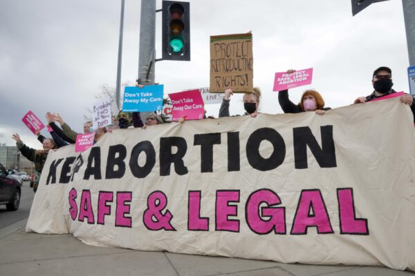 people hold up a large banner that reads "keep abortion safe and legal"