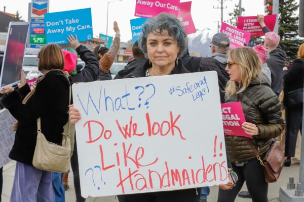 a person stands with a sign that reads "what?  do we look like servants?" in front of people at a rally