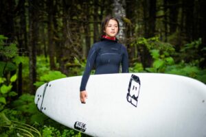 A young woman carrying a surfboard in the forest