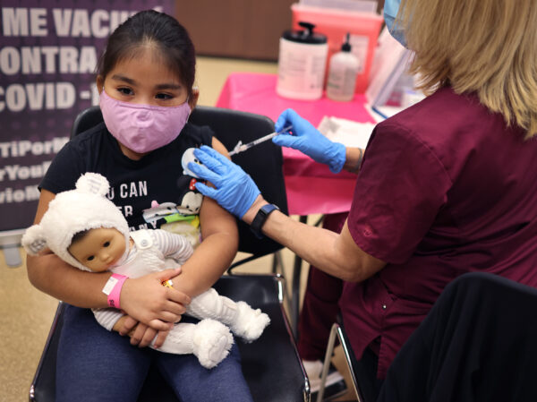 A child with a mask and a doll gets a shot