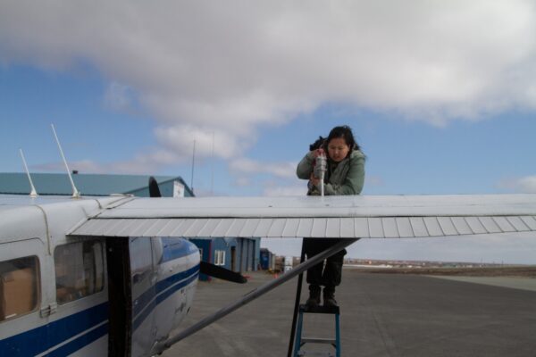 A woman standing on a ladder to refuel a plane