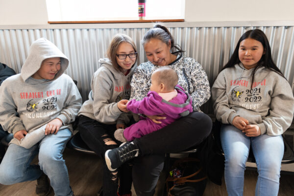An older woman and three teenagers hold a baby 