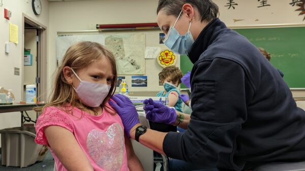 A girl in a pink shirt and mask gets a shot