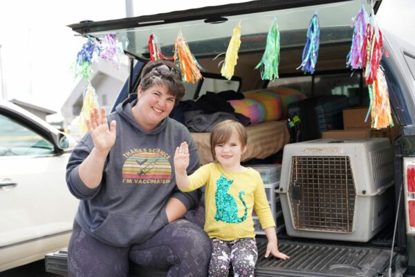 A woman and a child sit in the back of an SUV and wave