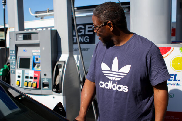 A man in a blue shirt puts gas in his car.