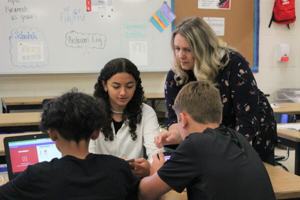 a woman talks to three students at desks