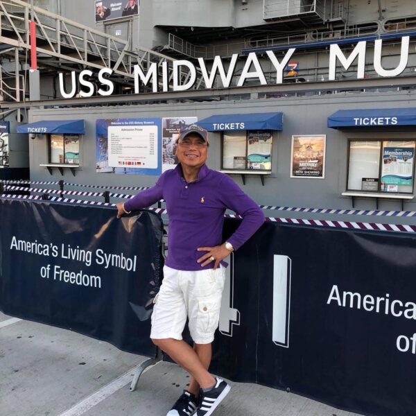 A man poses for a photo in front of a sign that says "USS Midway Museum"