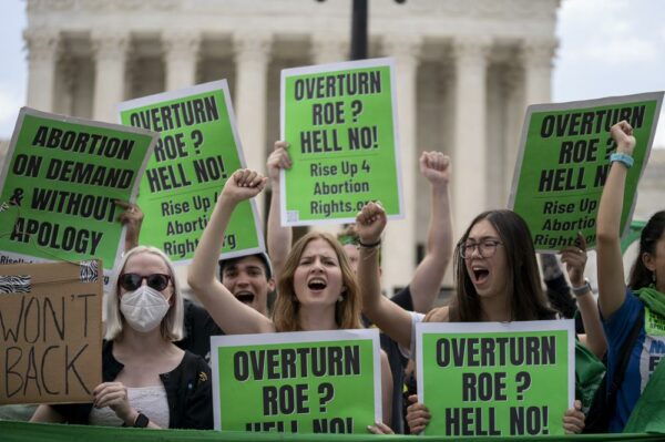 a group of people hold signs that say "Overturn Roe? Hell no!"