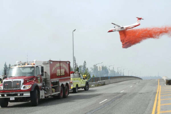 a plane drops red retardant on flames near a road